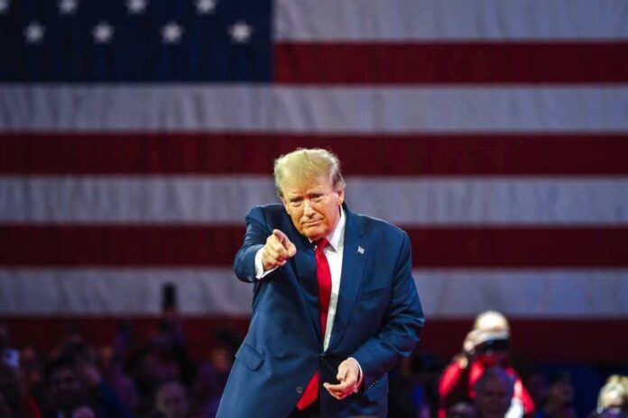 shutterstock_2455396913-1.jpg featured image Donald Trump in front of American flag pointing toward camera.
