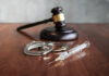 Gavel, handcuffs, and syringe on wooden table.