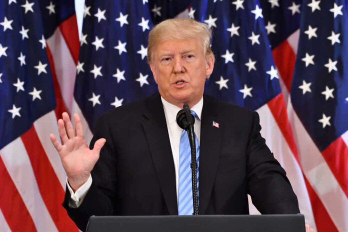 A man giving a speech with American flags behind.