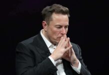 Man in black suit thinking with hands clasped.