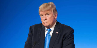 Man in suit with blue background speaking at podium.