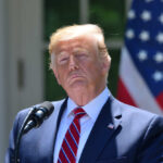 Donald Trump speaking with US flag in the back.