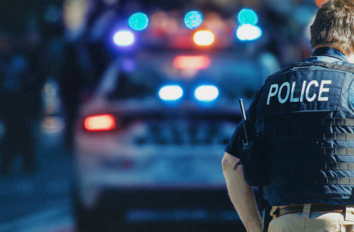 shutterstock_1543591088-1.jpg Police Officer Stands Near Patrol Car