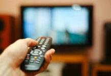 Hand holding a remote control towards a TV screen