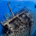 Divers exploring large underwater shipwreck in clear ocean