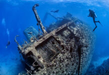 Divers exploring large underwater shipwreck in clear ocean