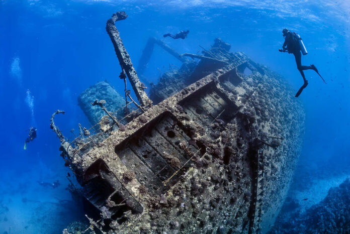 shutterstock_1961620324.jpg featured image Divers exploring large underwater shipwreck in clear ocean