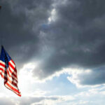 USA flag at half-mast under cloudy sky