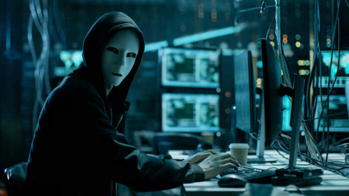 Person in hoodie and mask using computer