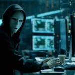 Massive CyberCrime BUST: Rapper Bot Taken Down Person in hoodie and mask using computer, multiple screens