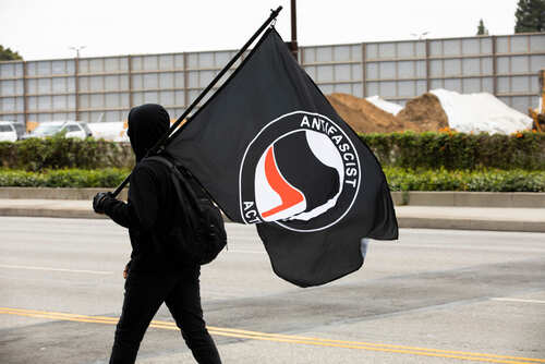 Person dressed in black clothing holding an Antifa flag