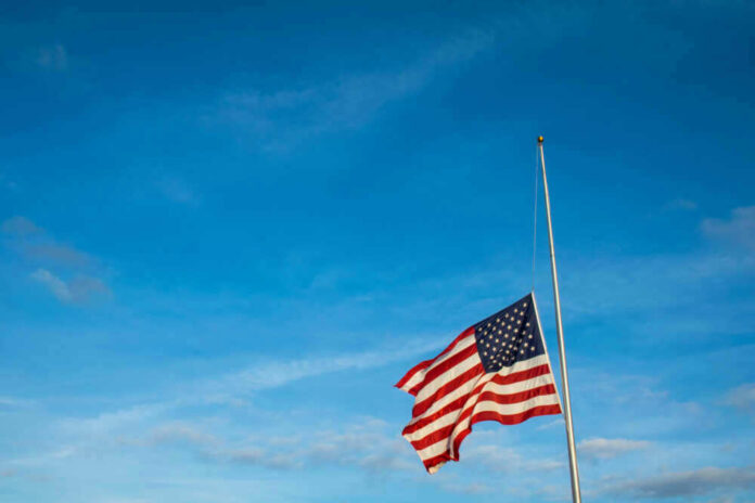 American flag at half-mast against a clear blue sky.