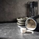 TOXIC Protein Powders EXPOSED — Half Contain Lead A black protein powder container with a scoop, weights, and a water bottle on a dark surface
