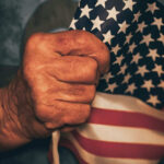 Trump DECLARES Victory Day — Leftists STUNNED Hand holding small American flag tightly.