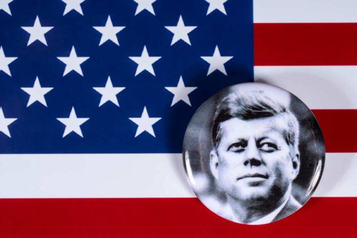 shutterstock_1081177643.jpg A black and white badge of John F. Kennedy on an American flag background