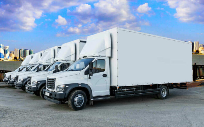 Line of white box trucks in parking lot.
