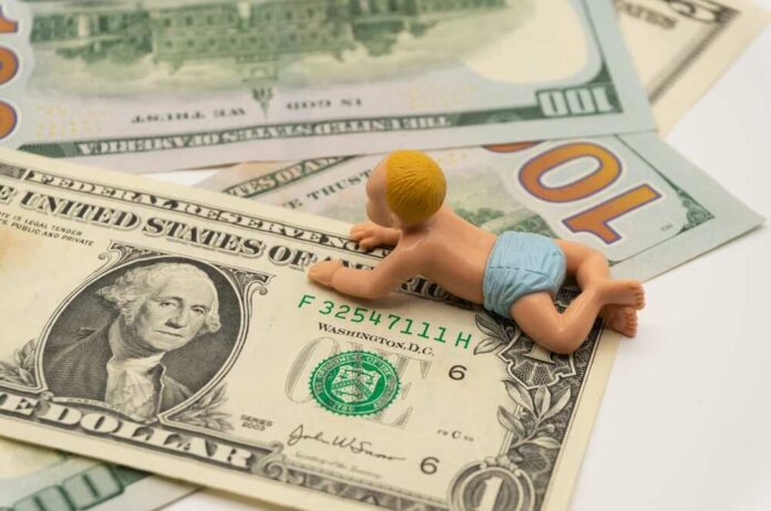 A baby figurine crawling on top of various dollar bills