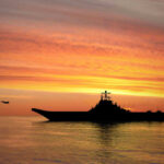Silhouette of an aircraft carrier at sunset.
