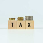 Blocks spelling 'TAX' with coins stacked beside them