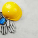 Yellow hard hat, measuring tape, and gloves on a gray surface