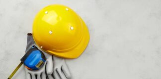 Yellow hard hat, measuring tape, and gloves on a gray surface