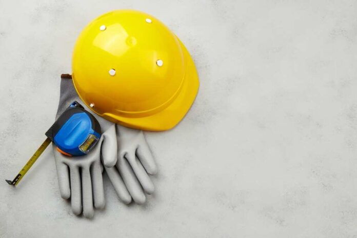 Yellow hard hat, measuring tape, and gloves on a gray surface
