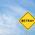 A yellow warning sign with the word 'BETRAY' against a blue sky