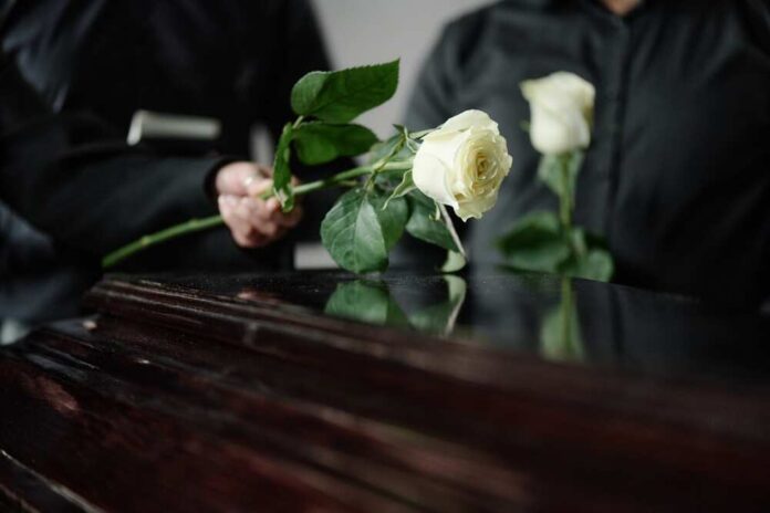 Two individuals placing white roses on a coffin during a funeral