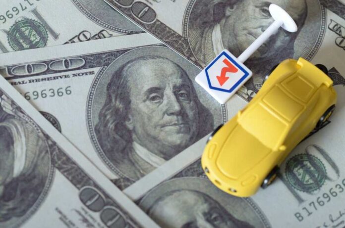 A yellow toy car on top of hundred dollar bills with a small directional sign
