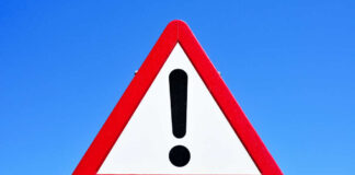 A triangular warning sign with an exclamation mark against a blue sky