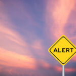 Yellow alert sign against a colorful sunset sky