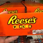A hand holding a box of Reese's Pieces candy in a grocery store