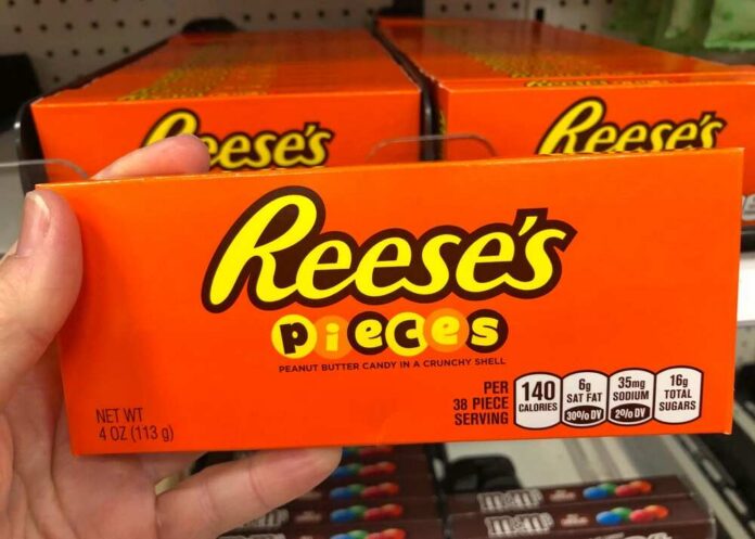 A hand holding a box of Reese's Pieces candy in a grocery store