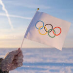 Hand holding Olympic flag in snowy landscape