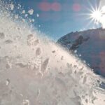 Snow spraying from a slope under a bright sun