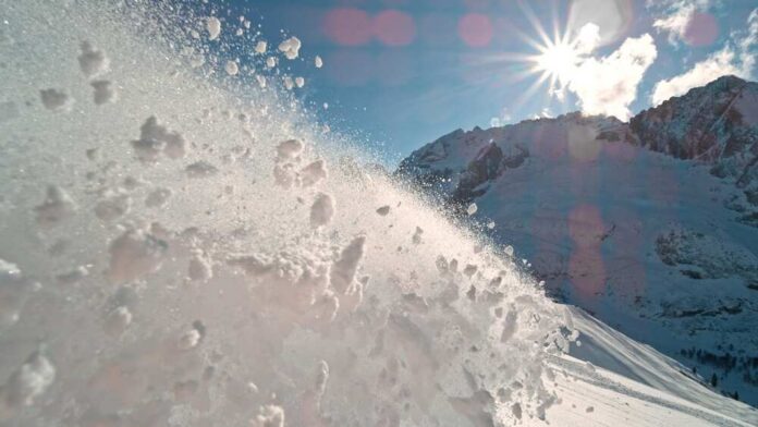Snow spraying from a slope under a bright sun