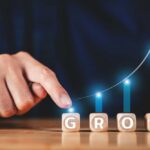 A hand pointing at wooden blocks spelling 'GROW' with a rising graph in the background