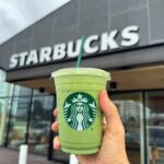 Hand holding a green matcha drink in front of a Starbucks store