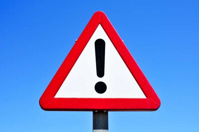 A triangular warning sign with an exclamation mark against a blue sky