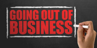 A hand writing 'GOING OUT OF BUSINESS' on a chalkboard