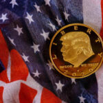 A gold commemorative coin featuring a profile of Donald Trump on an American flag background