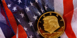 A gold commemorative coin featuring a profile of Donald Trump on an American flag background