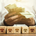 Person counting cash with wooden blocks depicting store icons