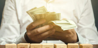 Person counting cash with wooden blocks depicting store icons