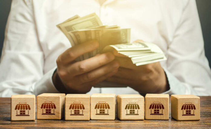 Person counting cash with wooden blocks depicting store icons