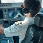 Pilot in cockpit wearing headphones and operating aircraft controls