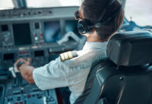 Pilot in cockpit wearing headphones and operating aircraft controls