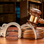 Wooden gavel and handcuffs on a table.