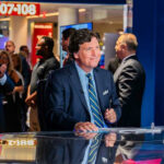 Tucker Carlson at news desk, people applauding in background.