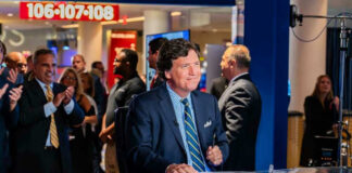 Tucker Carlson at news desk, people applauding in background.